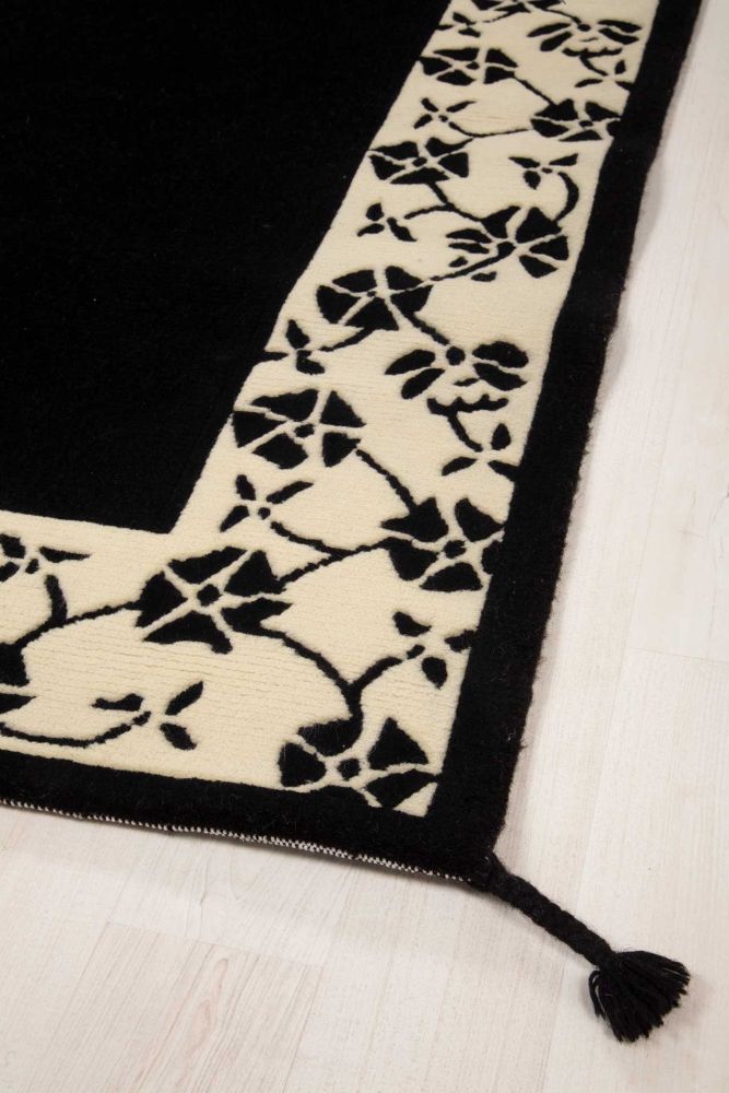 Handknuten ullmatta med enfärgat svart spegel och blombård i vitt och svart